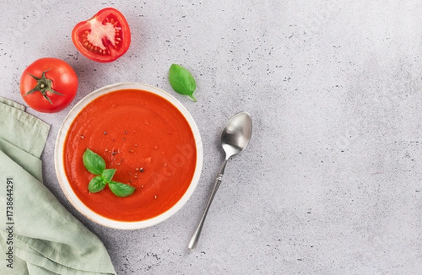 Fototapeta Bowl of tomato puree soup with fresh basil on grey background. Top view. Copy space. Vegan food.