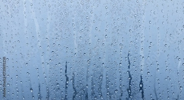 Obraz Close-up of water condensation on a cold glass window pane. Macro view of moisture droplets and streams creating an abstract blue texture background