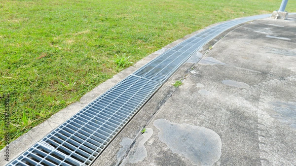 Fototapeta Steel grating covering a roadside drainage channel, creating a flat and even surface for safety, ensuring durability,