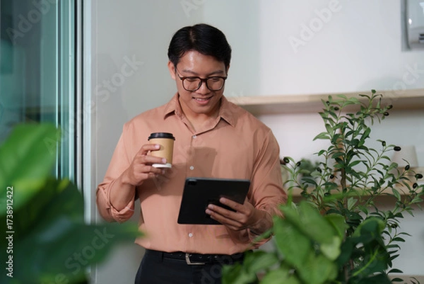 Fototapeta Young Professional Enjoying Coffee While Using Tablet in Green Office