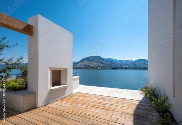 Obraz A contemporary outdoor space with a white wall, wooden decking, and lake views.  The design features a fireplace niche with a serene vista.
