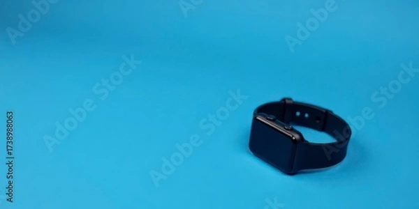 Fototapeta A Sleek Black Smartwatch Resting on a Vibrant Blue Background, Ready for Your Next Technological Adventure