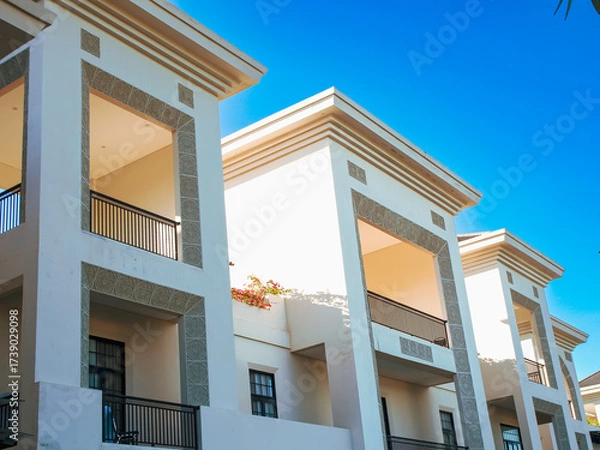 Fototapeta Exterior of building with elements of Art Deco or Mediterranean Revival architecture with clear blue sky background, low angle shot.. Modern apartment building with blue sky