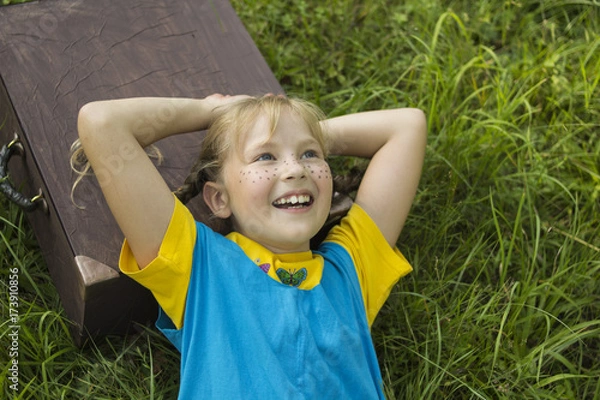 Obraz a fair-haired, freckled girl, lies on the grass, she has a suitcase under her head, she dreams of traveling.