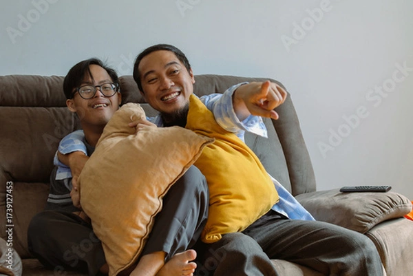 Fototapeta Joyful Father and Son with Special Needs Moment Sharing a Laugh While Watching TV Together at Home