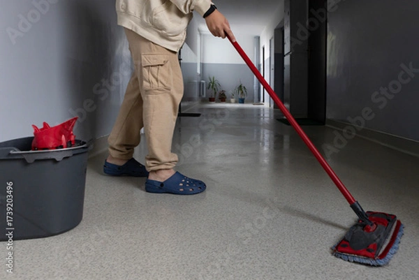 Fototapeta Person cleaning hallway with mop and bucket in a modern building during daytime hours