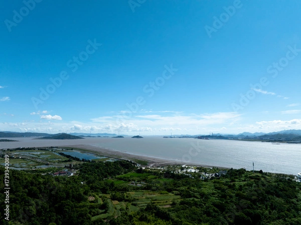 Fototapeta Aerial view of a coastal area with lush greenery, water, and distant islands
