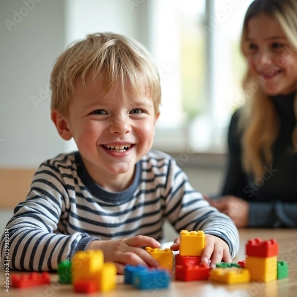 Fototapeta Happy child plays with colorful toy blocks during therapy session. Boy smiles joyfully. Parent or therapist supports learning development indoors. Playful activity promotes engagement and creativity.