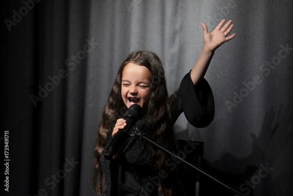 Fototapeta An artistic talented little girl singer takes the top note. An emotional singer and actress performs on stage.