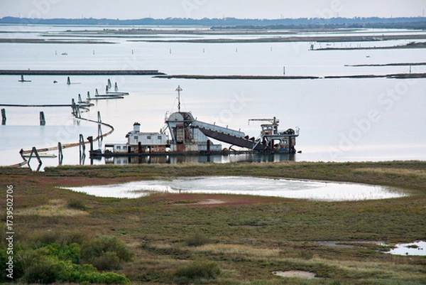 Fototapeta Industrial dredging machinery operates in a quiet coastal lagoon or marshland.