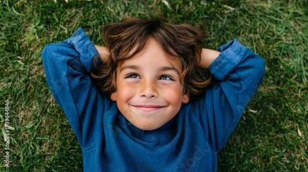 Fototapeta A young boy smiling while lying down in a grassy field.