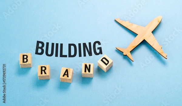 Fototapeta A wooden airplane is flying over a blue background with the letters Building Brand