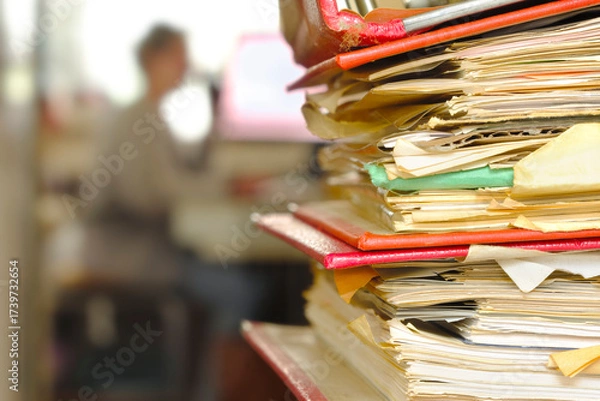 Obraz Stack of ring binders, file folders with workplace in the back. Beat the clock, deadlines, urgency, stress concept.Unrecognizable Person,free copy space.
