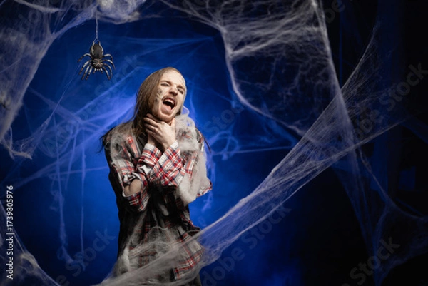 Obraz Creepy scary zombie man with ugly makeup shouting and suffocate because painful strangle health problem standing on spooky spider web background. Halloween. Horror film.