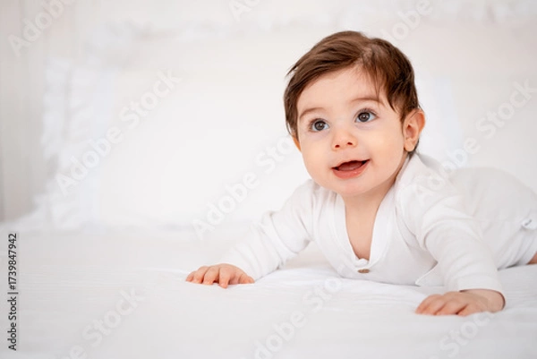 Obraz a baby on a white bed at home, a place for text, a cute smiling little child getting ready for bed, a portrait of a little boy child