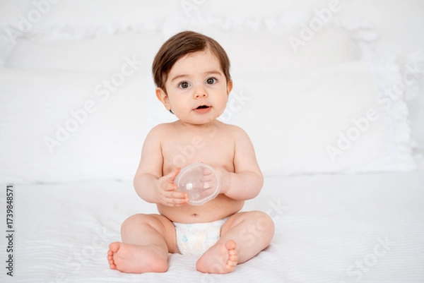Obraz A baby in diapers on a white bed at home, a place for text, a cute smiling little child