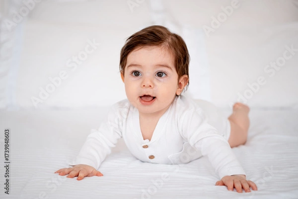 Obraz a baby on a white bed at home, a place for text, a cute smiling little child getting ready for bed, a portrait of a little boy child