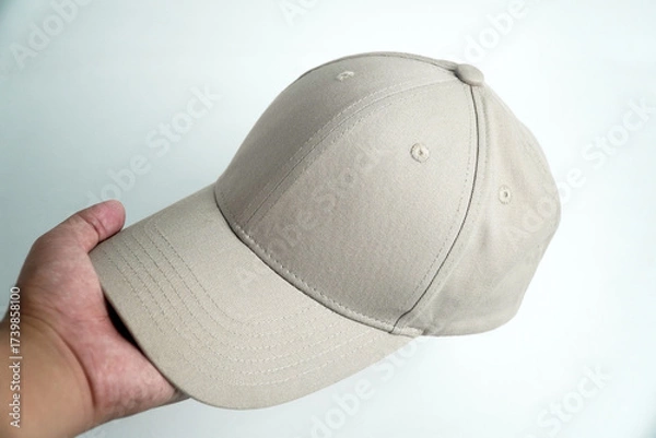 Fototapeta A hand holds a blank gray baseball cap, presenting it against a clean white background. This versatile image is perfect for mockups, clothing, or accessory concepts.