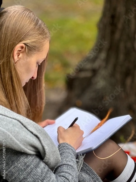 Fototapeta woman writes on a notebook in an autumn park