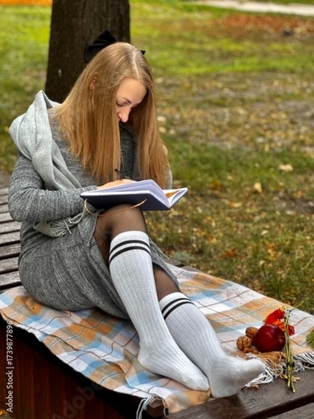 Fototapeta woman writes on a notebook in an autumn park
