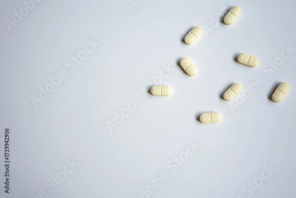 Fototapeta Scattered yellow tablets lie on a white background in a minimal arrangement. The image can be used to illustrate healthcare, medication, treatment, or pharmaceutical concepts.