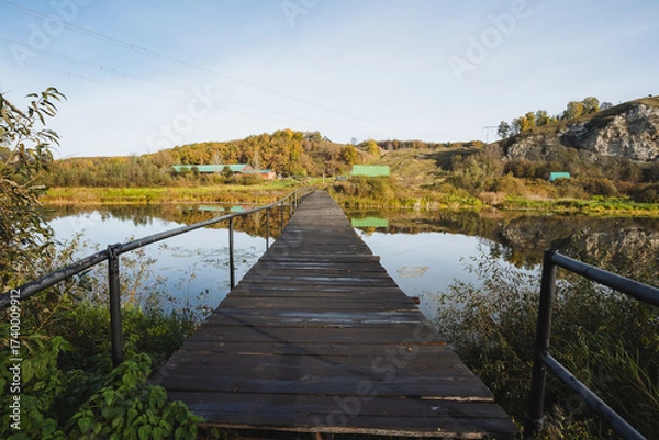 Fototapeta A charming wooden pier extends over a peaceful river in the countryside, especially stunning in autumn, ideal for relaxation and reflection, offering moments to unwind and enjoy natures tranquility
