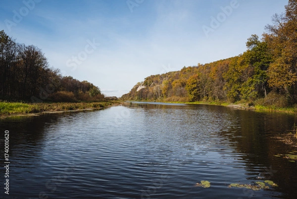 Fototapeta  The landscape of the serene autumn river, surrounded by lush green hills, creates a perfect backdrop for relaxation and adventure alike. This idyllic setting invites exploration and escape
