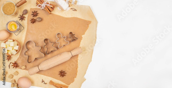 Fototapeta Christmas gingerbread dough with cookie cutters, rolling pin, spices and ingredients on parchment paper with copy space top view