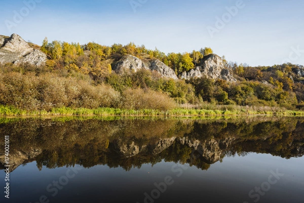 Fototapeta A Serene Autumn Landscape Beautifully Reflecting in the Calm Waters of the River, Showcasing the Tranquil Essence of Nature and the Idyllic Foliage During This Peaceful Season of Transition
