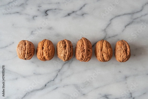 Fototapeta Close-up of walnuts in their shells lined up on white marble