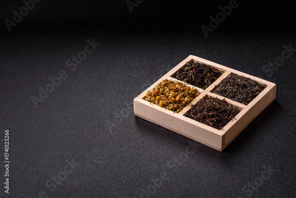 Fototapeta A wooden box with several types of dried tea, green, black, fruit, and chamomile. Dry tea in the box