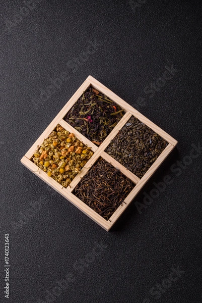 Fototapeta A wooden box with several types of dried tea, green, black, fruit, and chamomile. Dry tea in the box