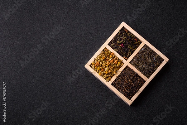 Fototapeta A wooden box with several types of dried tea, green, black, fruit, and chamomile. Dry tea in the box