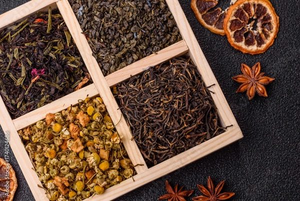 Fototapeta A wooden box with several types of dried tea, green, black, fruit, and chamomile. Dry tea in the box