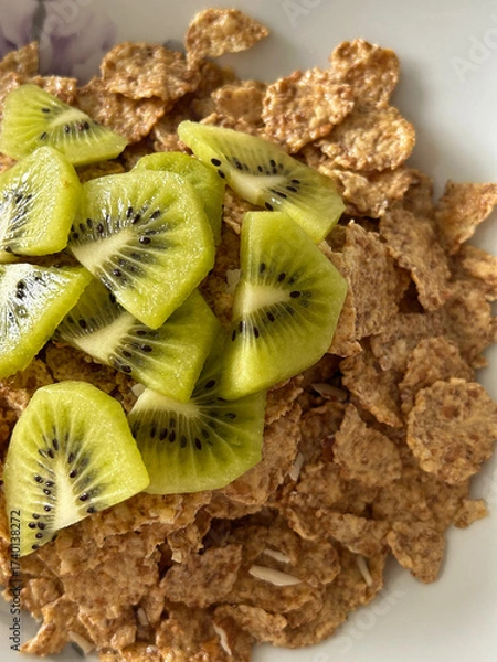 Fototapeta A close-up image showing a bowl of breakfast bran flakes topped with freshly sliced kiwi fruit.