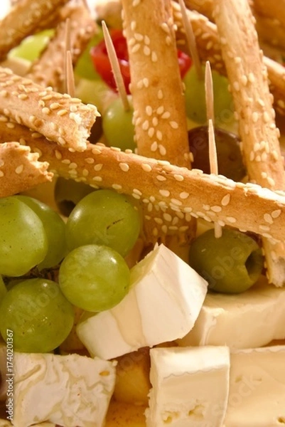 Obraz  Assorted brie cheese with grapes and olives, decorated with sesame breadsticks, served as an appetizer on a festive table.