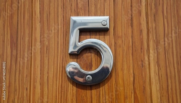 Fototapeta Close-up of a Shiny Metal Number 5 Mounted on a Wooden Surface