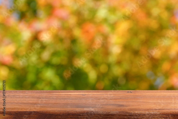 Fototapeta Empty wooden table on the background of autumn trees. Bright autumn colors in the garden. Free place for creativity.