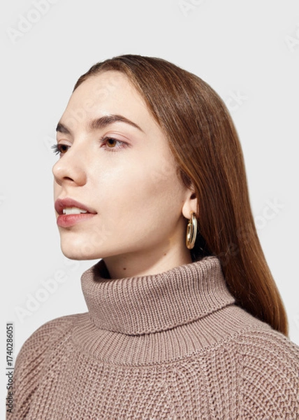 Fototapeta A beautiful woman in a beige knitted sweater poses on a gray background