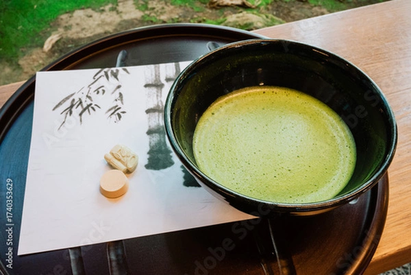 Fototapeta A bowl of frothy green matcha tea is served with traditional Japanese sweets on artistic paper. The image represents Japanese tea ceremony, culture, and mindfulness.