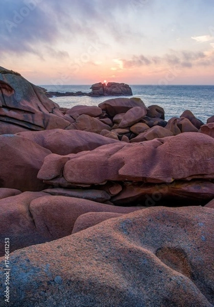 Fototapeta Stunning sunset over the Pink Granite Coast in Brittany, France. Unique weathered rock formations and ocean waves create a magical seascape in soft evening light.