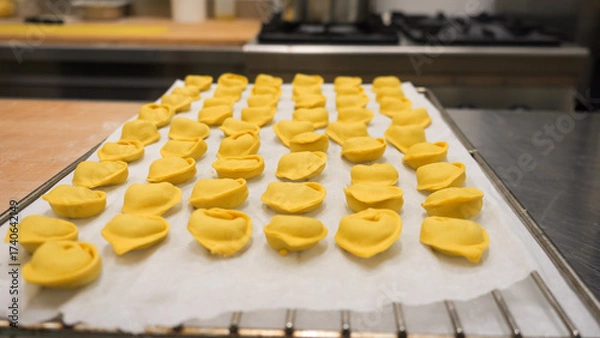 Fototapeta Artisan chef meticulously crafts fresh tortellini by hand with focused concentration in a bustling professional kitchen environment showcasing dedication to authentic Italian cuisine preparation