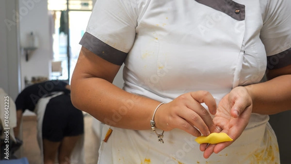 Fototapeta Skilled hands meticulously crafting small tortellini pasta in a bright professional kitchen showing dedication to authentic Italian culinary traditions and artisanal food preparation