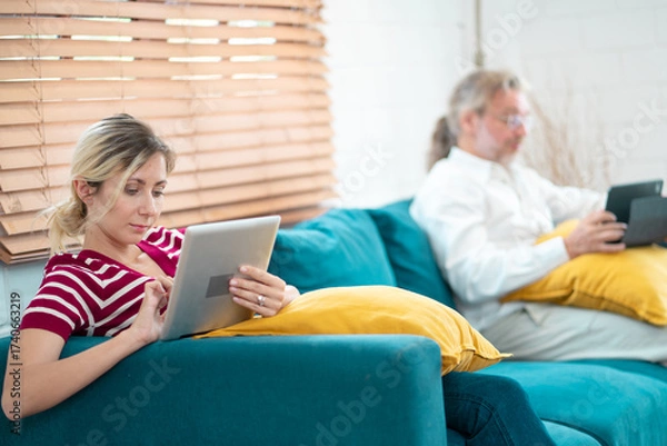 Fototapeta Young woman and grandfather using digital tablet at home. Freelancer holding and using digital tablet, sitting at cozy sofa in living room. Online technology. Remote job