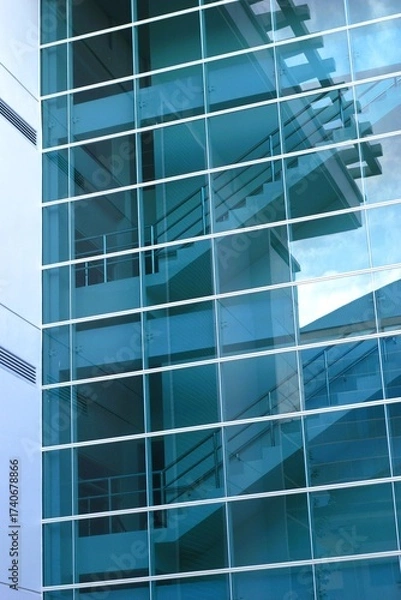 Fototapeta Modern glass building facade with reflections of staircase and structure