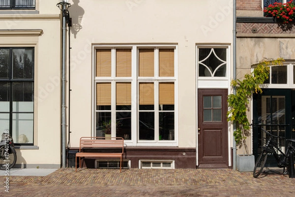 Fototapeta Charming European architecture with neutral facade, window, bench, door, plants, and brick path.