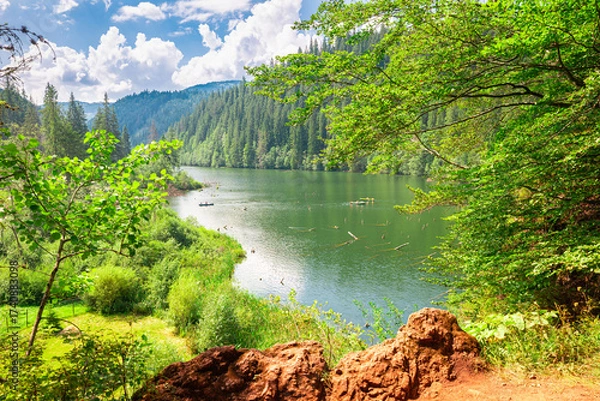 Fototapeta Scenic Red Lake (Lacul Rosu) in the eastern Carpathians, Romania, surrounded by lush forests and mountains in bright summer light.