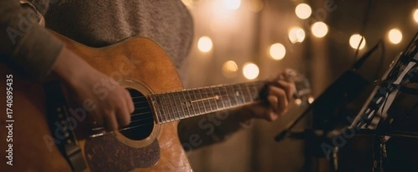Fototapeta The acoustic guitar in hands of musician performing intimate live set with warm bokeh lights