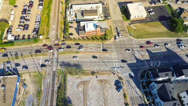 Fototapeta Railroad tracks and Cooper Street corridor in Arlington, Texas during peak traffic, flat-roof retail buildings, new development townhomes, mixed-use district with strong commuter and student flow