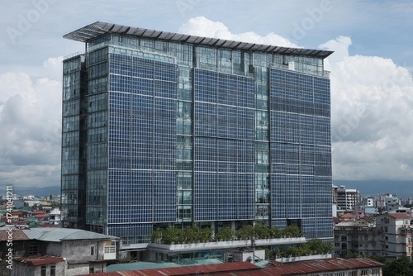 Fototapeta Modern office building with solar panels across the skyline in an urban setting during a cloudy day